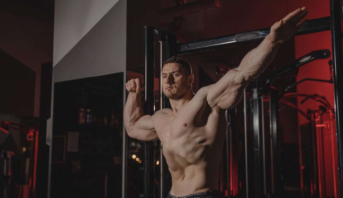 Strong and muscular man posing topless in a gym, showcasing fitness and strength.